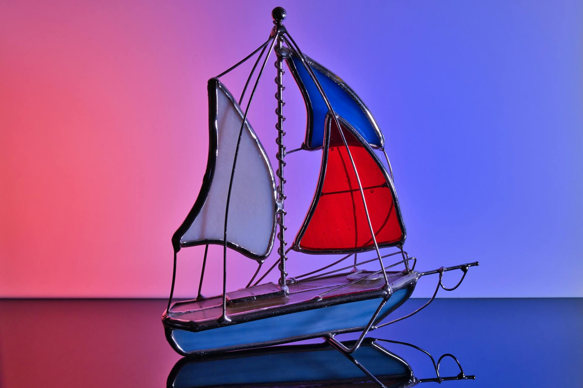 A colorful stained glass sailing ship with vibrant red and blue sails against a gradient background.