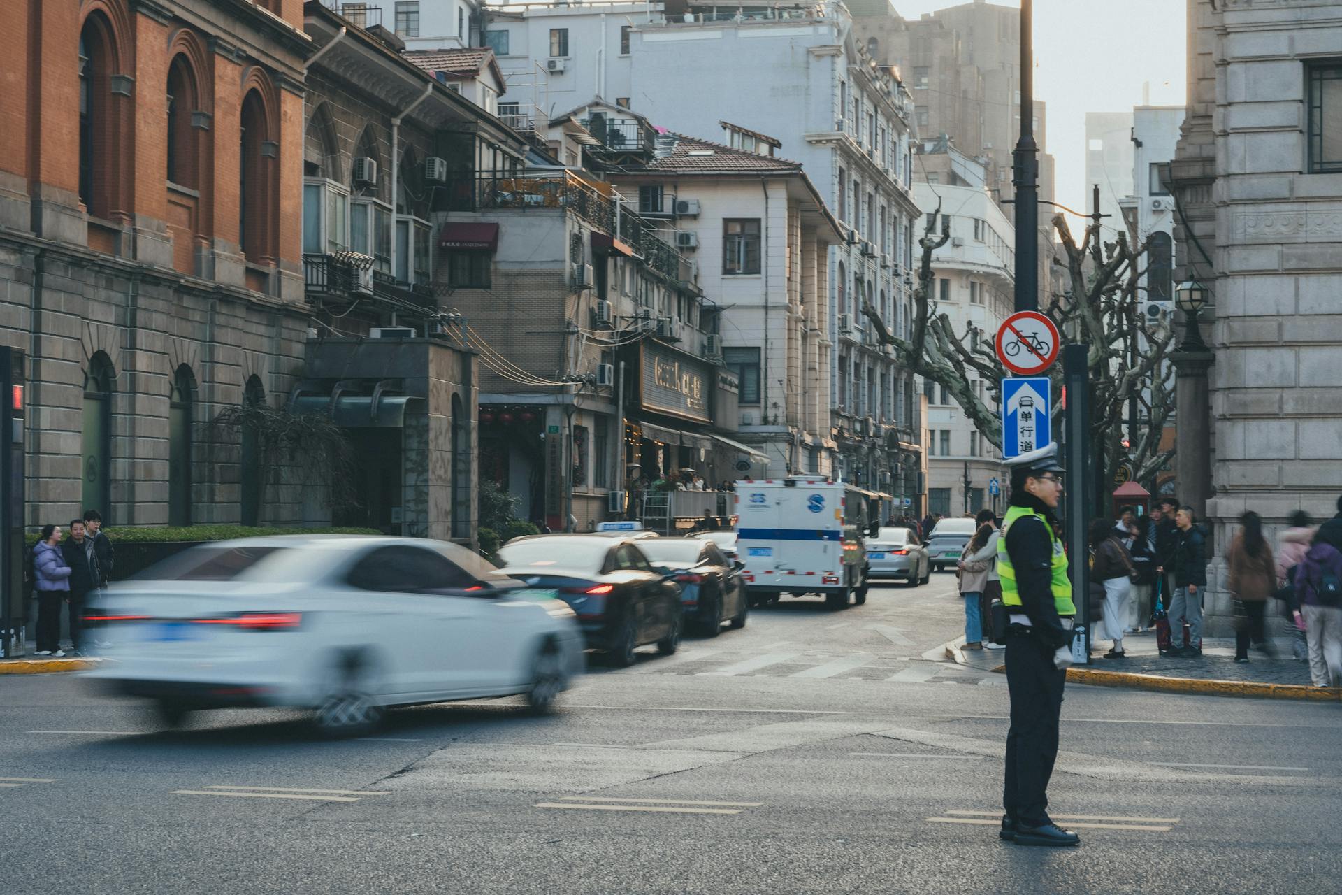 An urban street bustling with cars and people, featuring a traffic officer directing vehicles in a vibrant cityscape.