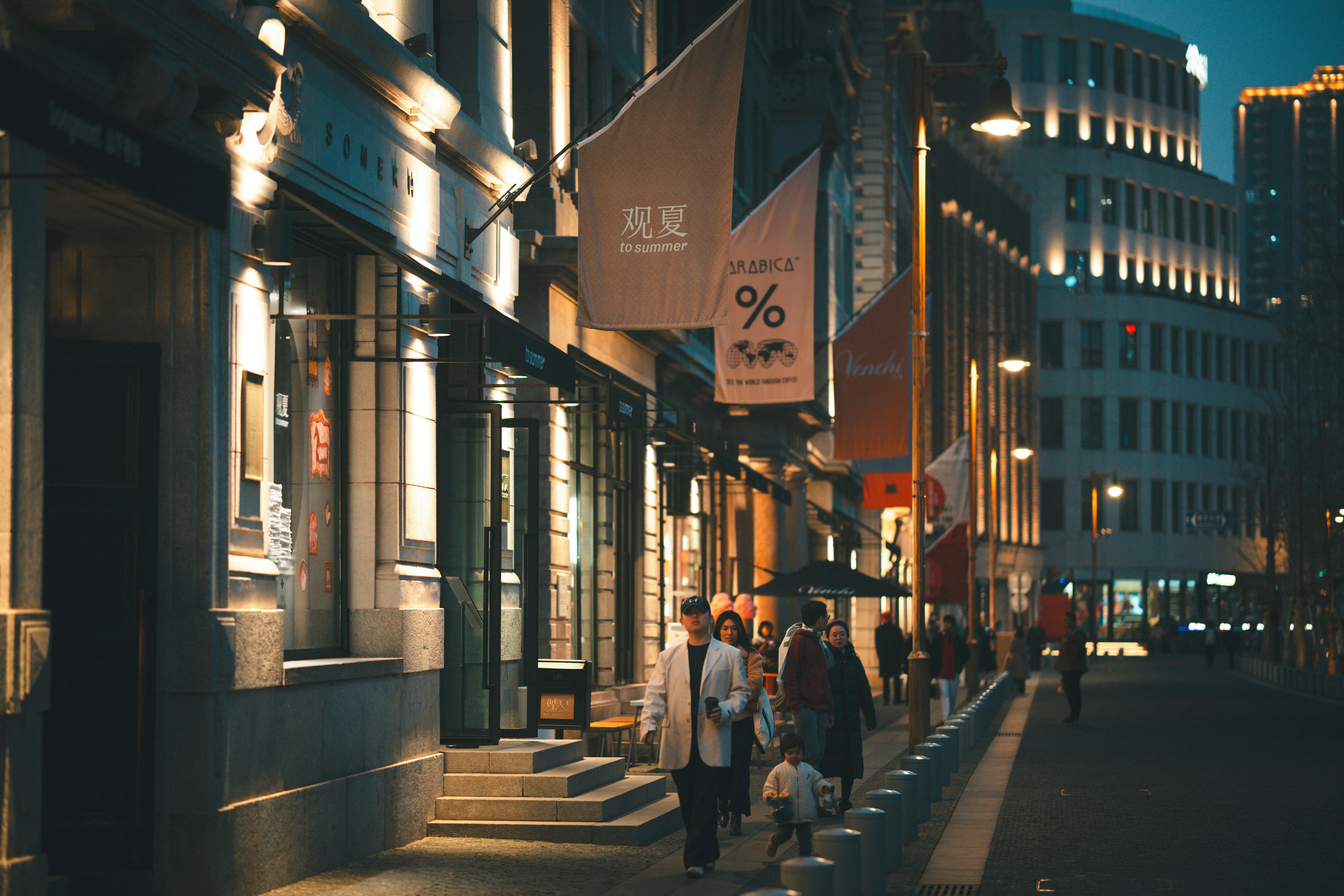 People strolling through a bright, illuminated street at night in an urban area.