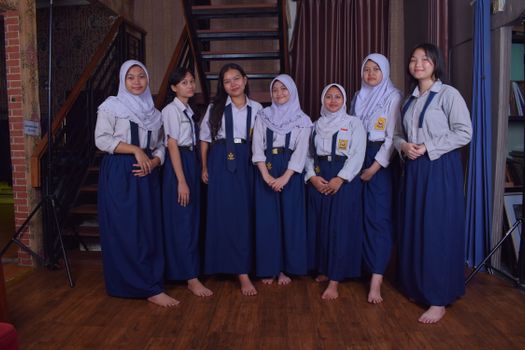 Seven female students in traditional school uniforms posing in an indoor setting with a staircase backdrop.