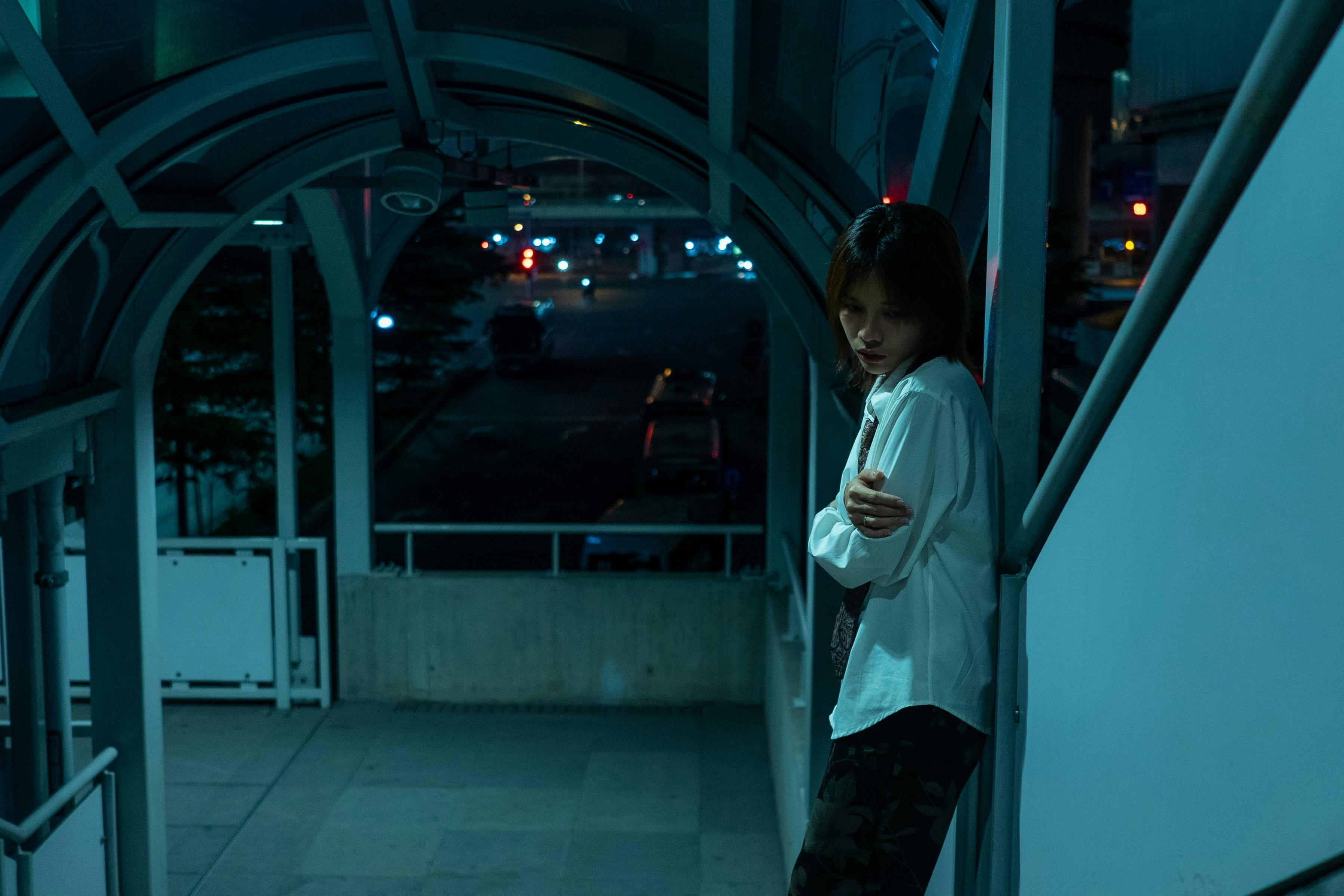 Gratuit Une jeune femme contemplative pose dans un décor nocturne urbain sous un éclairage bleu. Photos