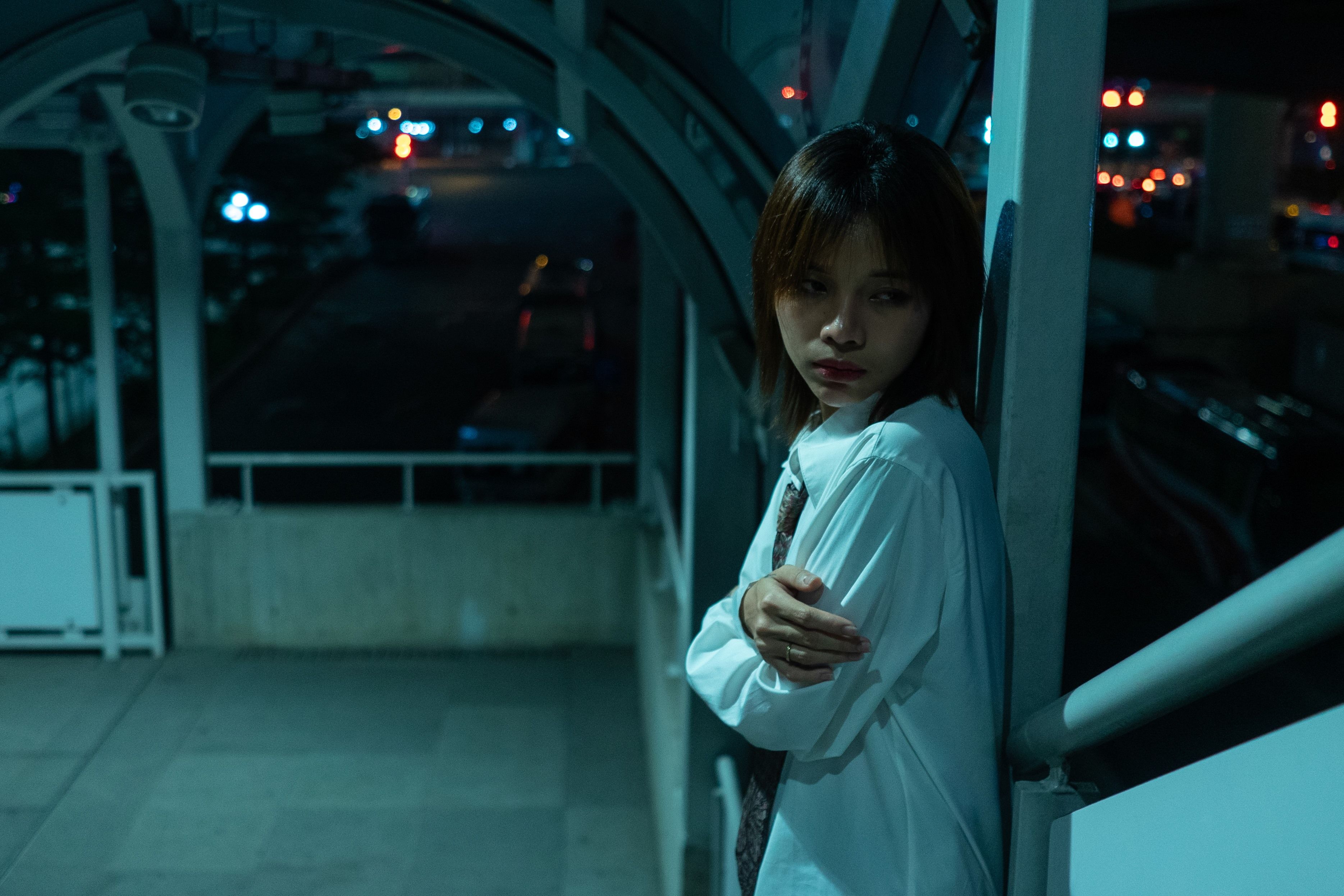 物思いにふける若い女性が夜の都会の歩道に立っており、憂鬱な雰囲気を醸し出しています。