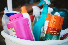 Close-up of assorted cleaning supplies in a bucket outdoors, showcasing various detergents and sprays.