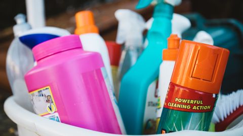 Close-up of assorted cleaning supplies in a bucket outdoors, showcasing various detergents and sprays.