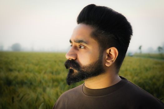 Side profile portrait of a man with a beard standing in a lush green field under daylight.