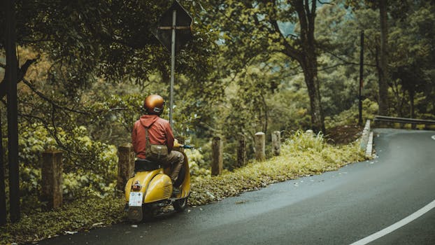 A person on a yellow Vespa takes a scenic road trip through lush greenery in East Java, Indonesia.