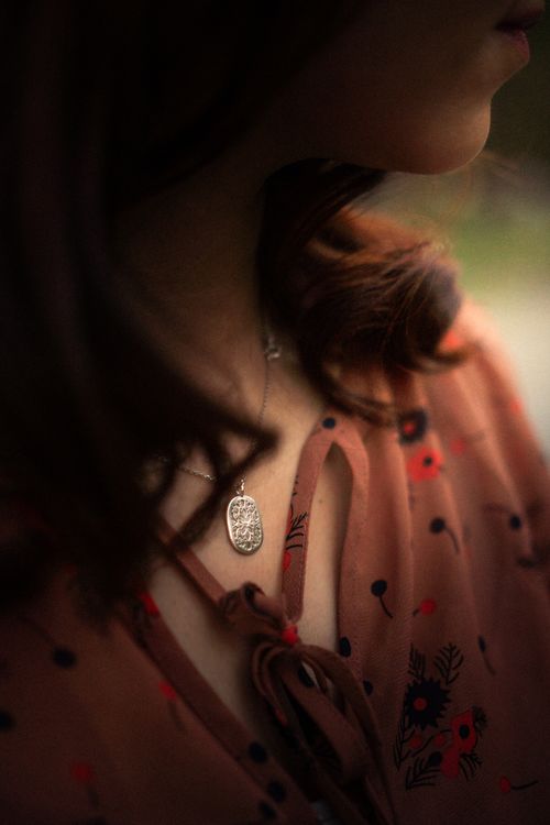 Free Close-up of a woman wearing a floral dress and elegant necklace, showcasing soft and warm tones. Stock Photo