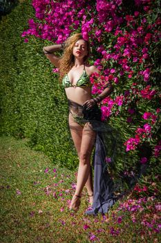 Elegant woman in floral bikini poses against vibrant pink flowers outdoors.