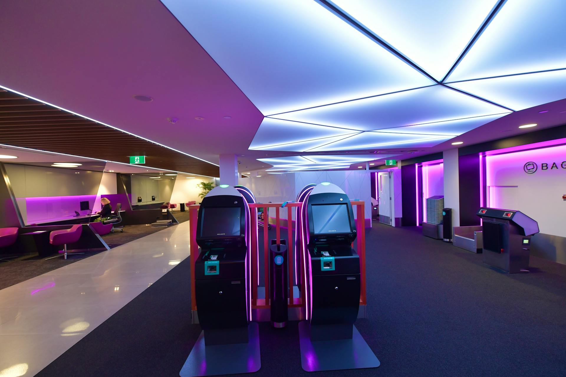 Stylish airport lounge featuring automated check-in machines and vibrant lighting.