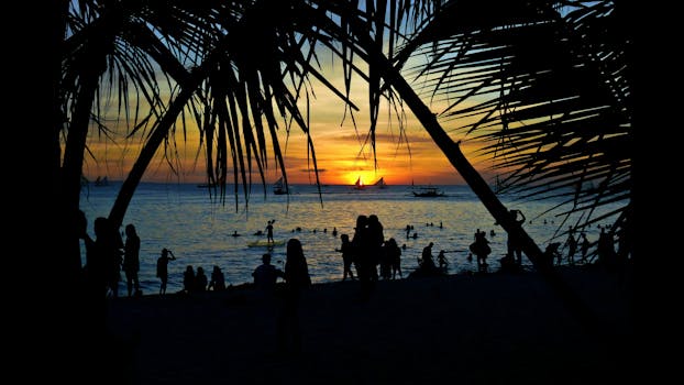 Silhouetted figures enjoy a vibrant sunset at Boracay's scenic shore in the Philippines.