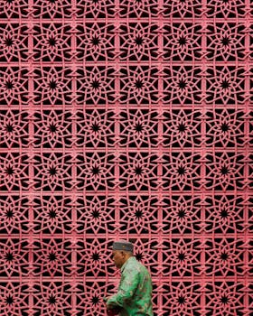 A man walks past a decorative lattice wall in Jakarta, Indonesia, showcasing urban culture and traditional attire.
