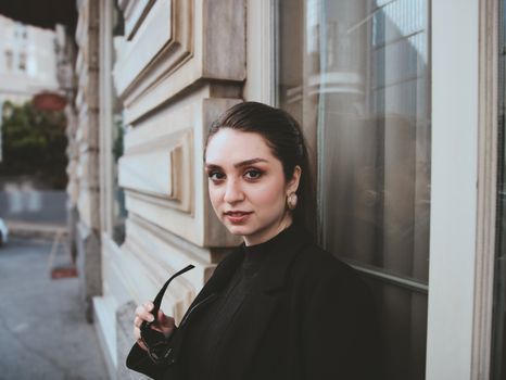Young woman in stylish black outfit standing by a building outdoors.