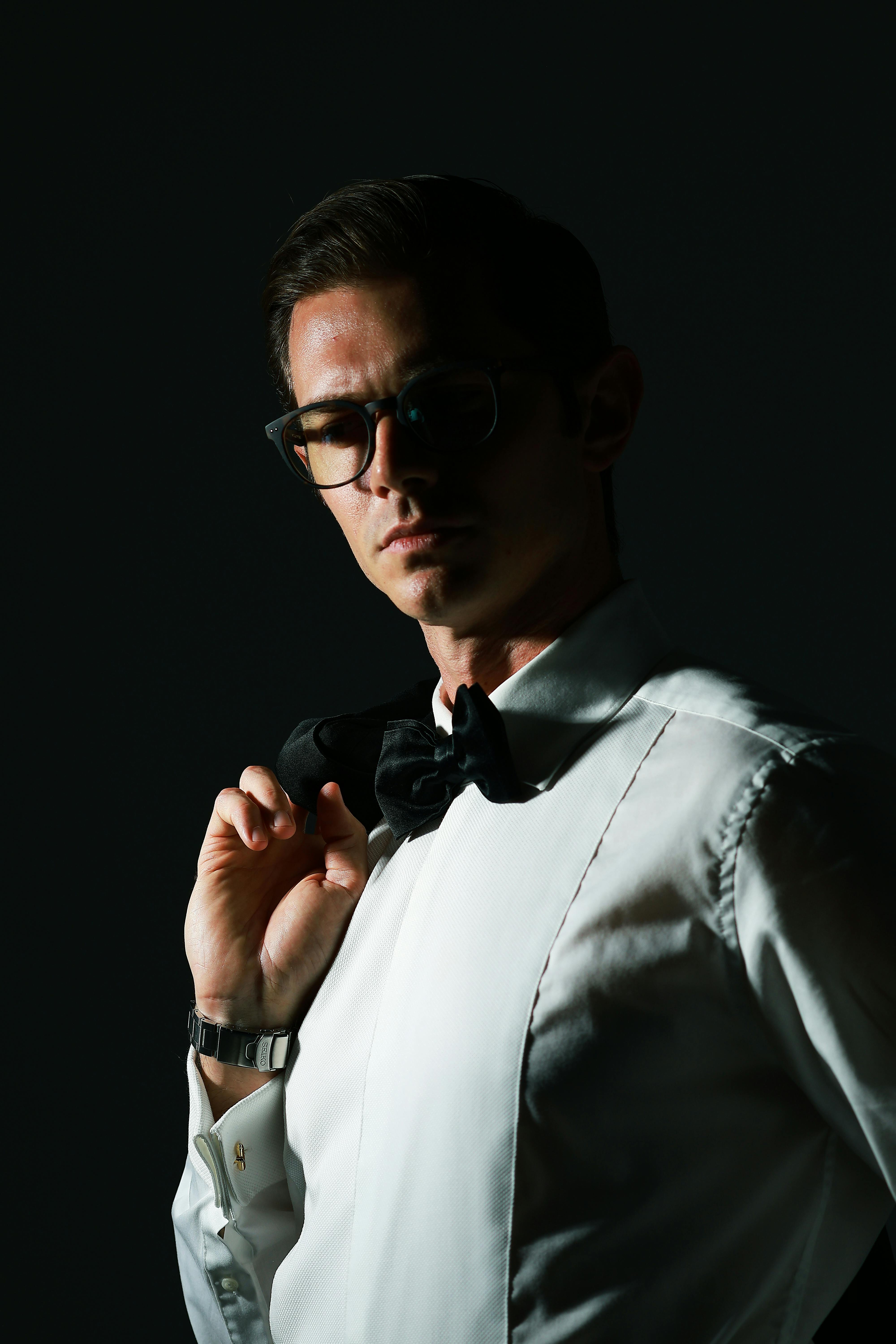 免費 在戲劇性的燈光下，一位戴著眼鏡、身穿燕尾服和領結的男子的肖像。 圖庫相片