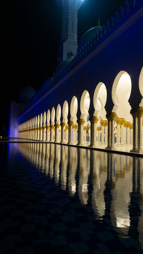 Free Elegant arches of a grand mosque reflected in calm water at night, creating a serene atmosphere. Stock Photo