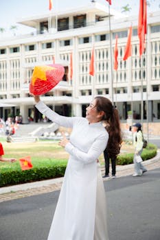 Woman in traditional dress joyfully holds Vietnamese conical hat in a festive setting.