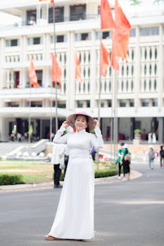 Woman in white traditional dress and hat in front of historic building with flags.