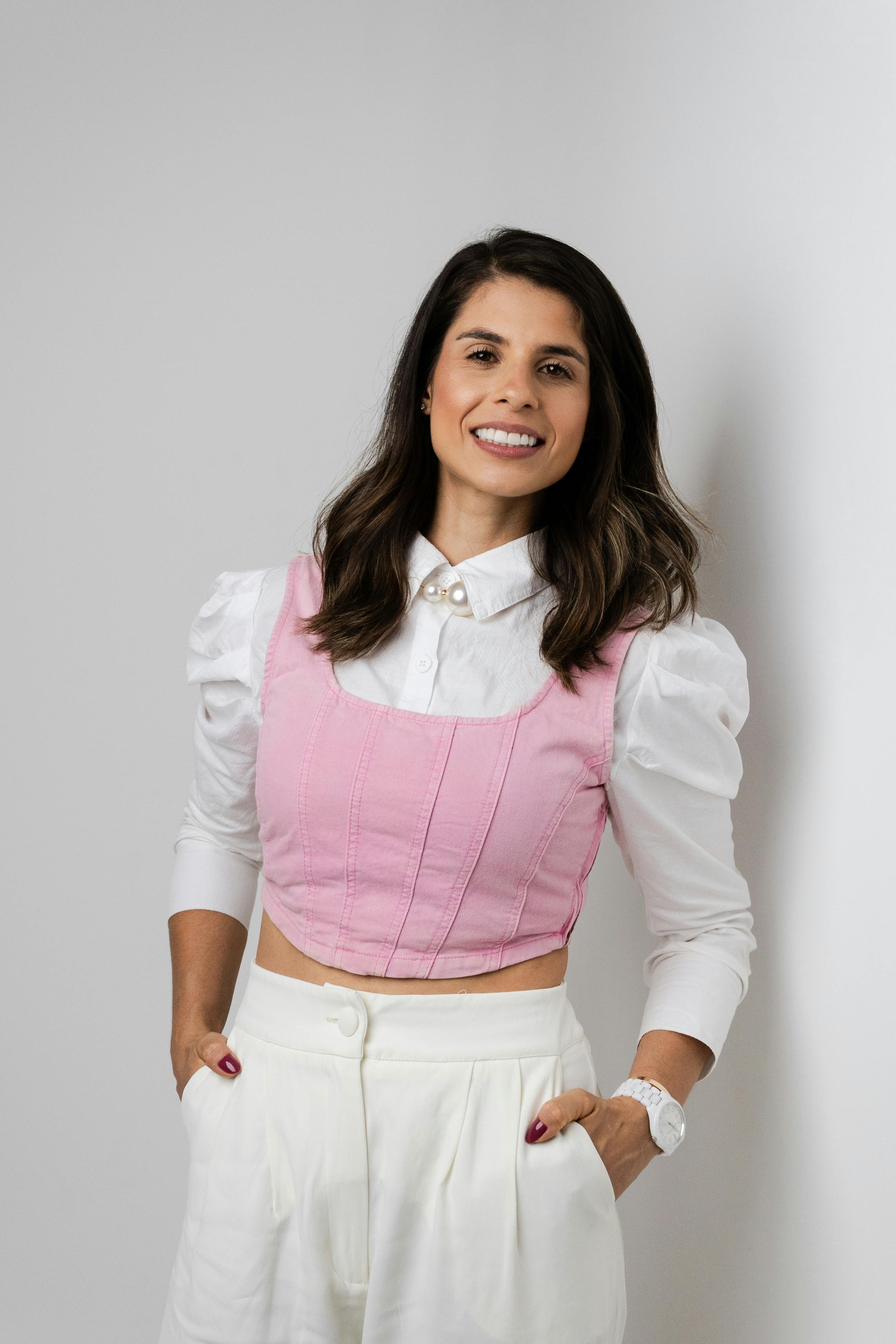 Portrait of a smiling woman in a stylish pink vest and white shirt, posing confidently.