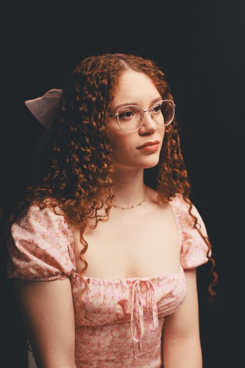 Free Charming portrait of a woman with curly hair in a pink dress, wearing glasses, exuding elegance and warmth. Stock Photo