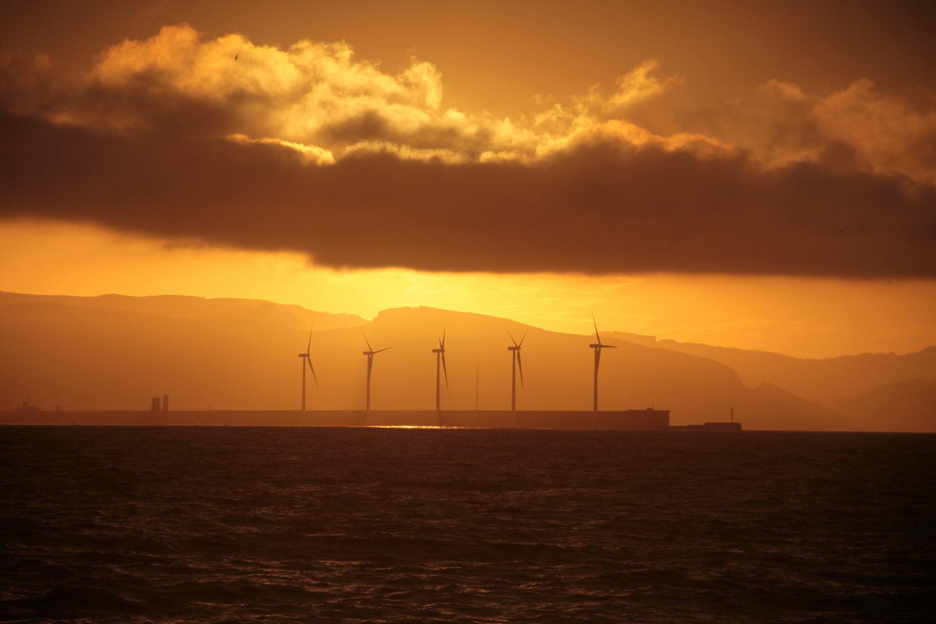 Silhouette of offshore wind turbines against a dramatic golden sky at sunset.