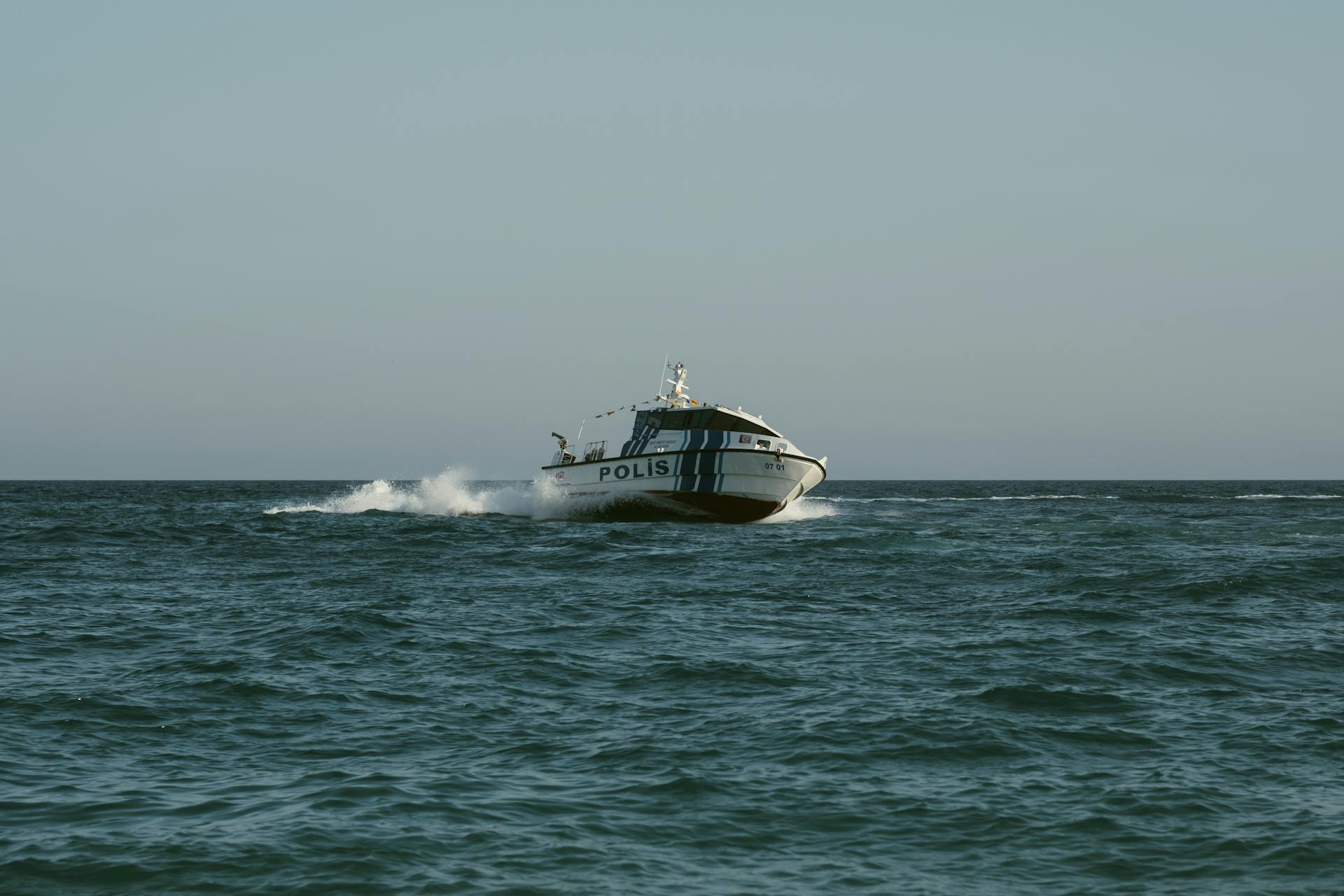 A police boat speeds across the open sea under clear skies, maintaining maritime security.