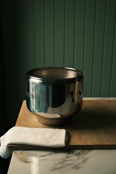 A stainless steel bowl rests on a wooden cutting board with a towel, creating a domestic kitchen scene.