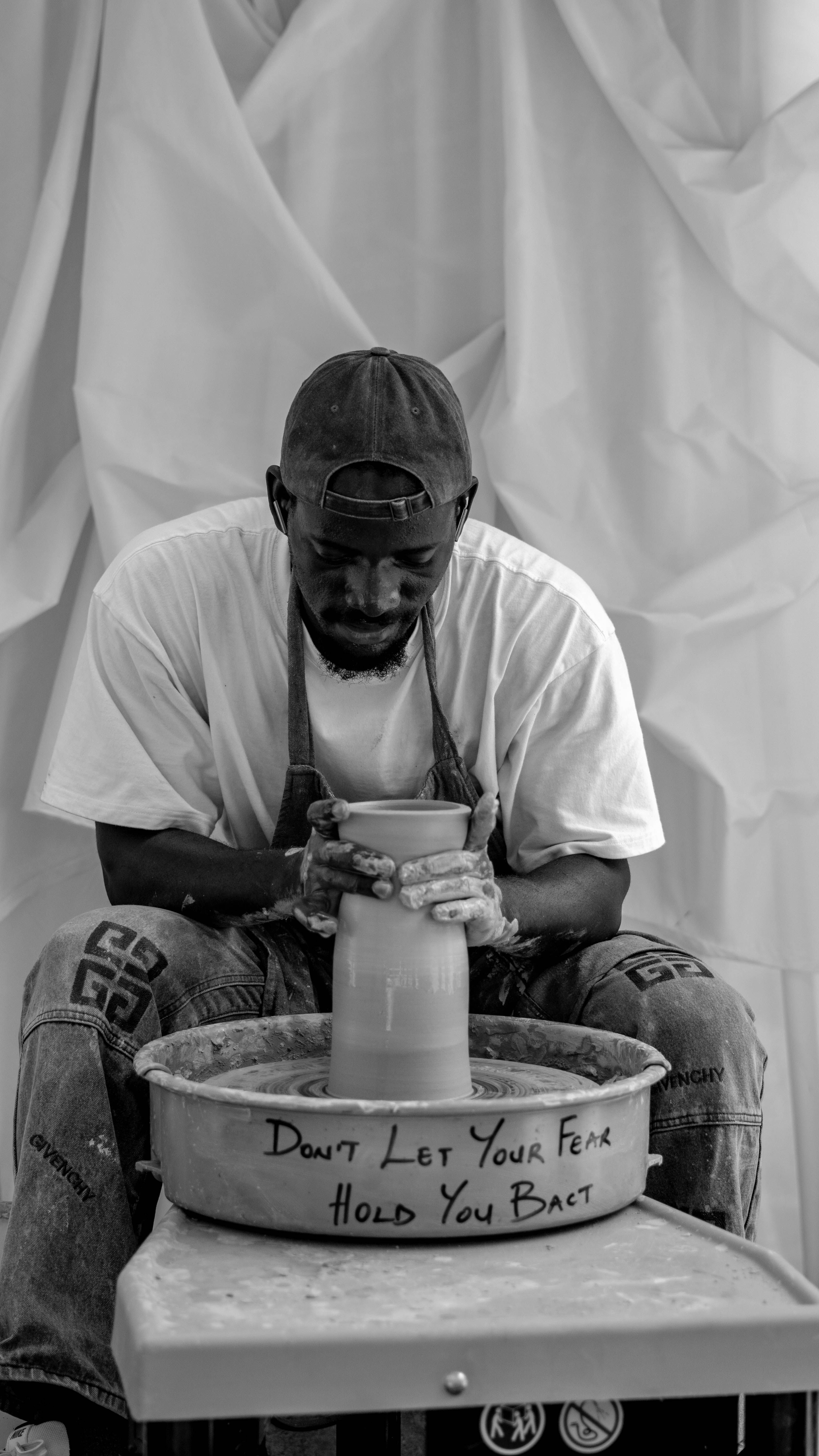 Man crafting pottery on wheel with inspiring message in rustic studio.