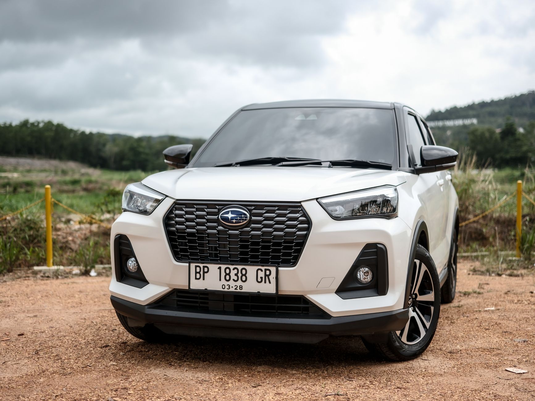 A modern white SUV parked on a dirt road, showcasing its sleek front design under a cloudy sky.
