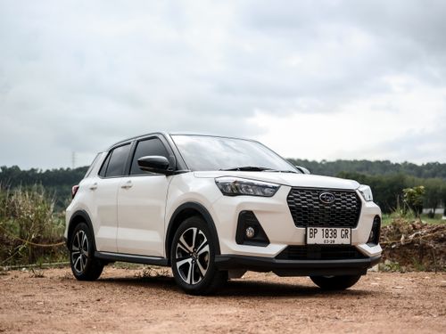Free A white compact SUV parked outdoors with greenery and cloudy sky backdrop. Stock Photo