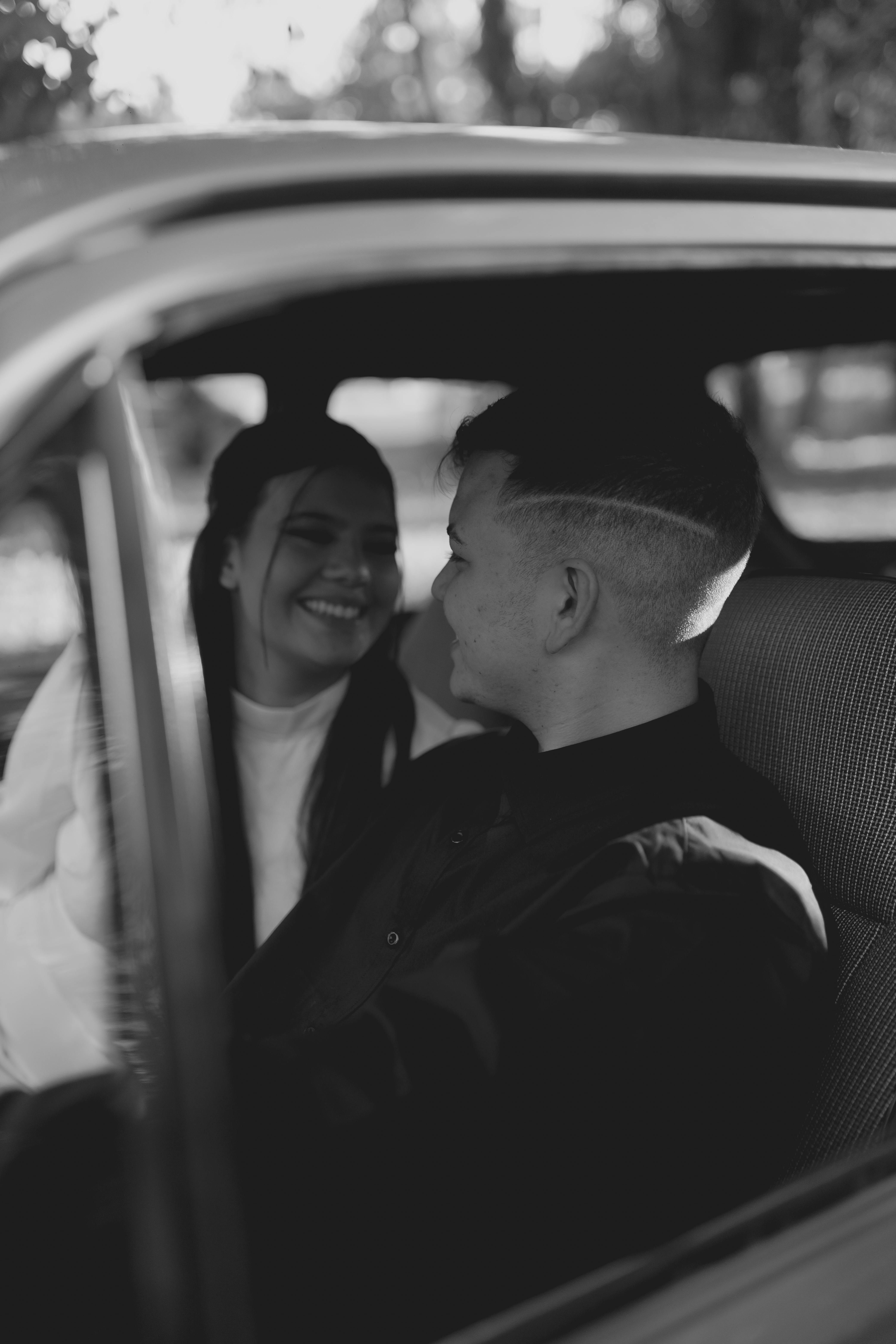 Smiling couple sitting inside a vintage car captured in a black and white photograph.