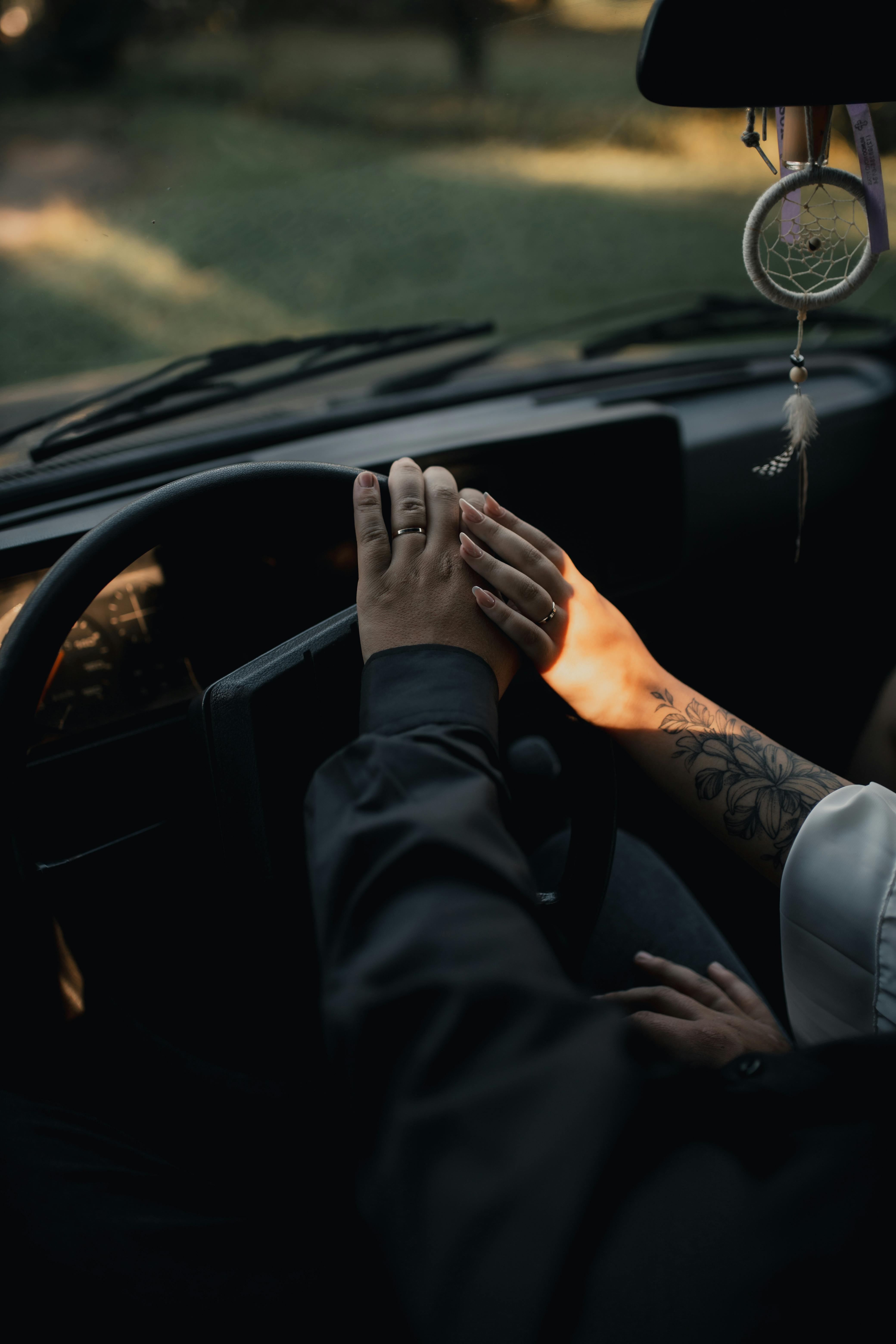 A romantic moment captured with a couple holding hands inside a car, featuring soft sunlight.