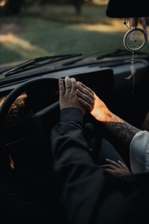 Free A romantic moment captured with a couple holding hands inside a car, featuring soft sunlight. Stock Photo