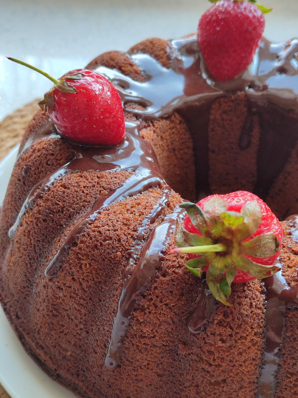 Chocolate bundt cake drizzled with glossy ganache and topped with whole fresh strawberries