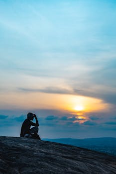A person observes a vibrant sunrise from a rocky hill in Abuja, Nigeria.