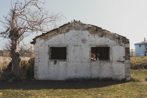 Free Old, crumbling house and bare tree under clear sky in peaceful rural setting. Stock Photo