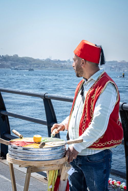 Free Turkish ice cream vendor in traditional attire serves by the Bosphorus in Istanbul. Stock Photo