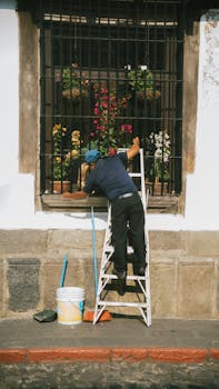 A man cleans a window in Antigua Guatemala, showcasing vibrant flowers and colonial architecture.