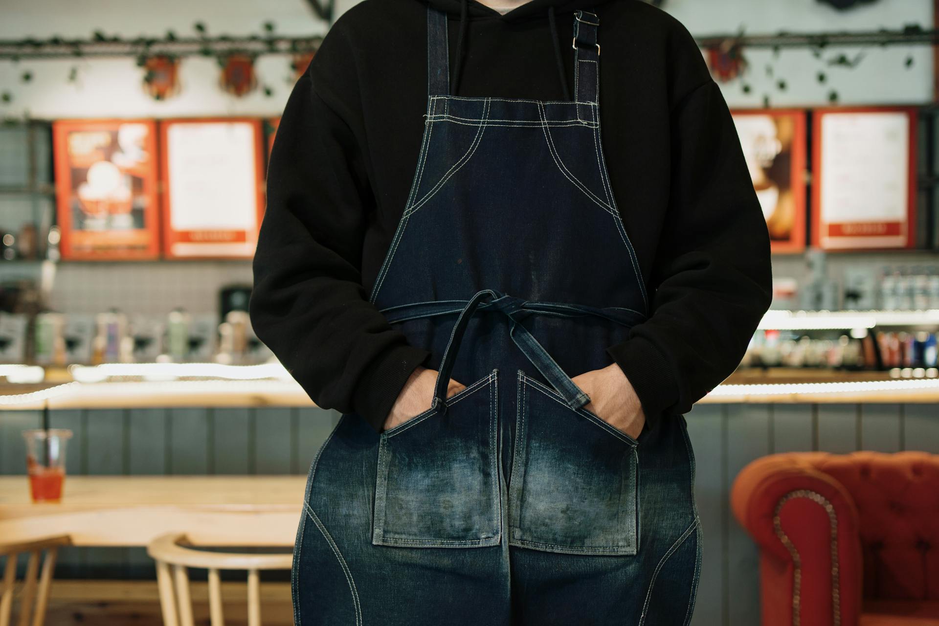 A barista stands in a cafe wearing a denim apron, creating a cozy and welcoming atmosphere.