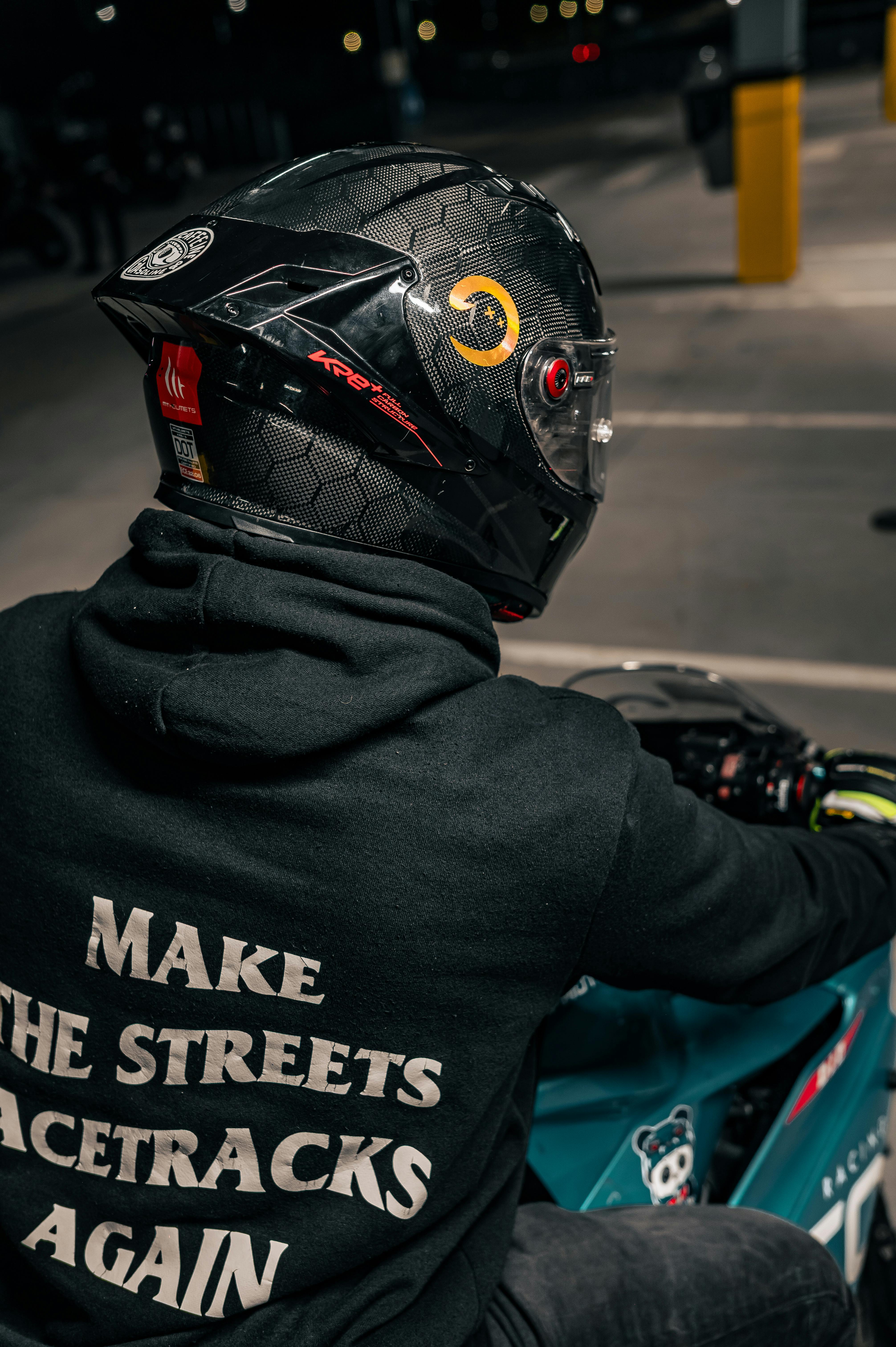 Free Back view of a biker wearing a helmet and a 'Make the Streets Racetracks Again' hoodie indoors at night. Stock Photo