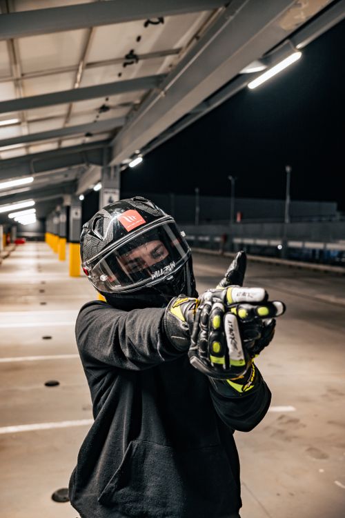 Free Motorcyclist wearing helmet and gloves posing in an urban parking area at night. Stock Photo