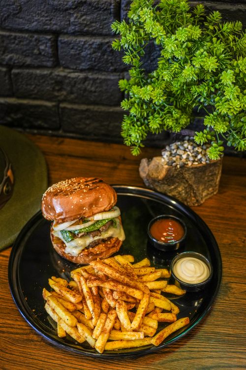 Free Gourmet cheeseburger with crispy fries accompanied by dipping sauces on a stylish black plate. Stock Photo