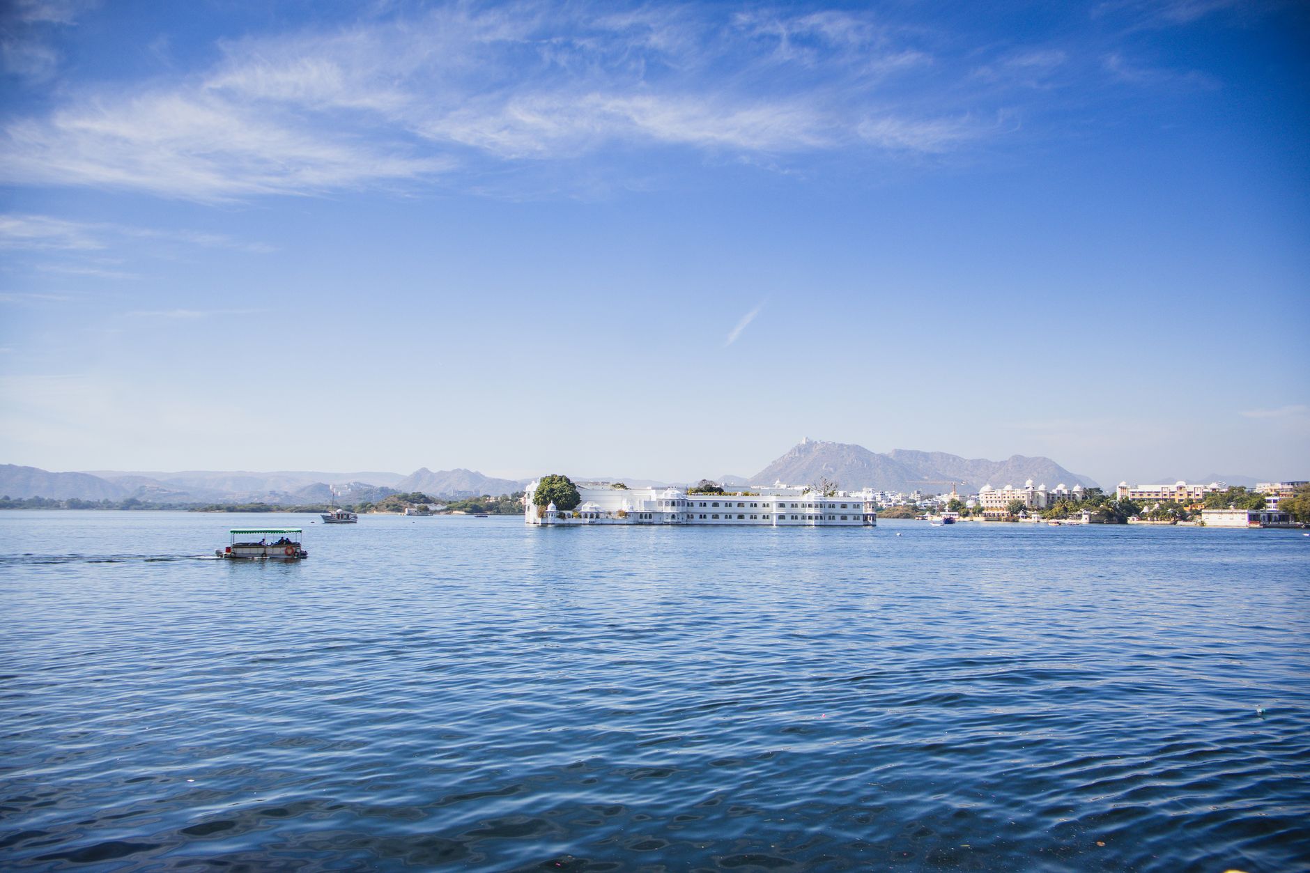A serene view of Lake Pichola in Udaipur with City Palace in the background under a clear blue sky.