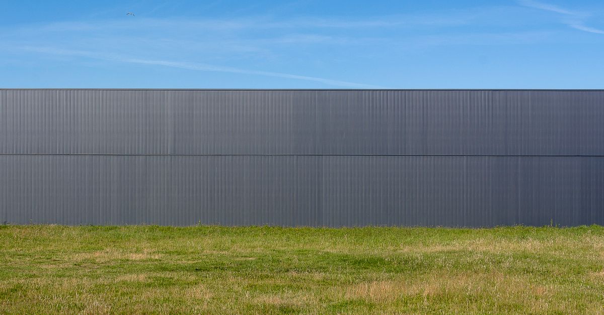Moderne Metallwand hinter dichtem Gras unter klarem blauem Himmel