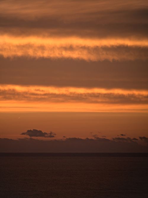Free A peaceful sunrise scene with glowing clouds over a calm sea horizon, setting a warm, serene mood. Stock Photo