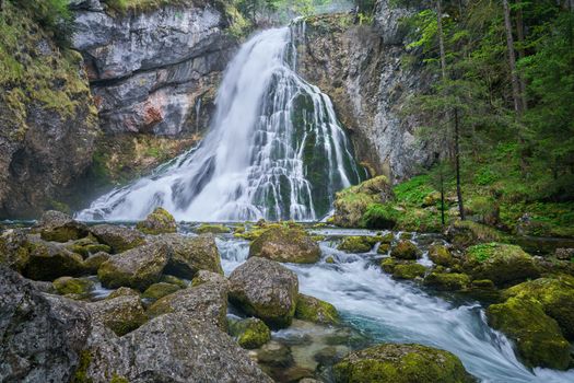 Gollinger Waterfall cascades down rocks surrounded by vibrant green forest in Austria.