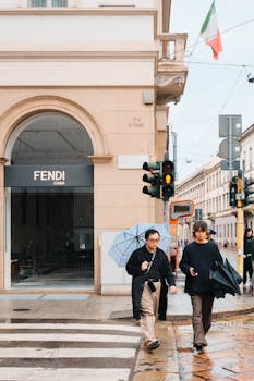 Two people walking in rainy Milan with umbrellas, showcasing urban life and fashion.