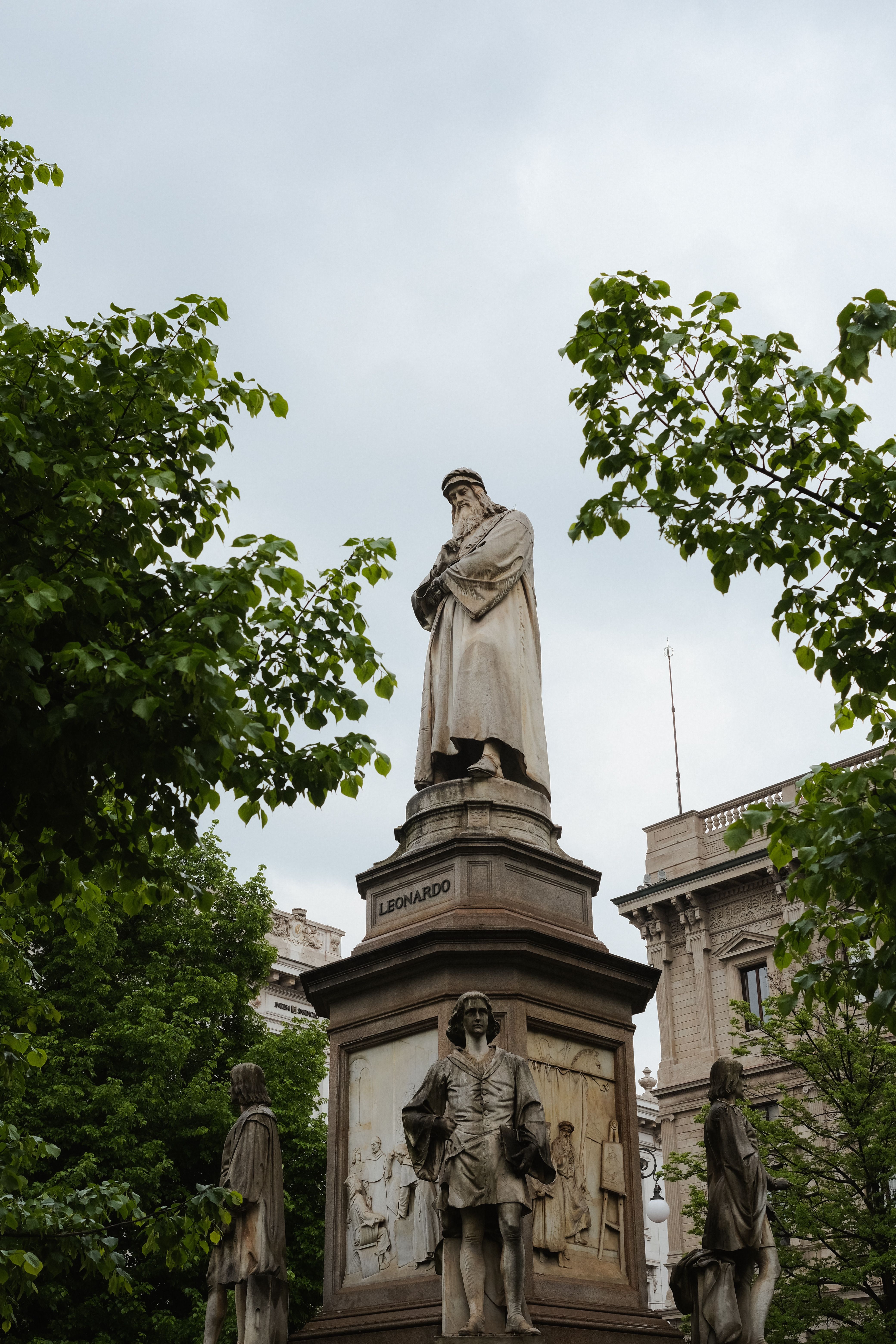 A grand view of Leonardo da Vinci statue in Milan's vibrant city center surrounded by lush greenery.