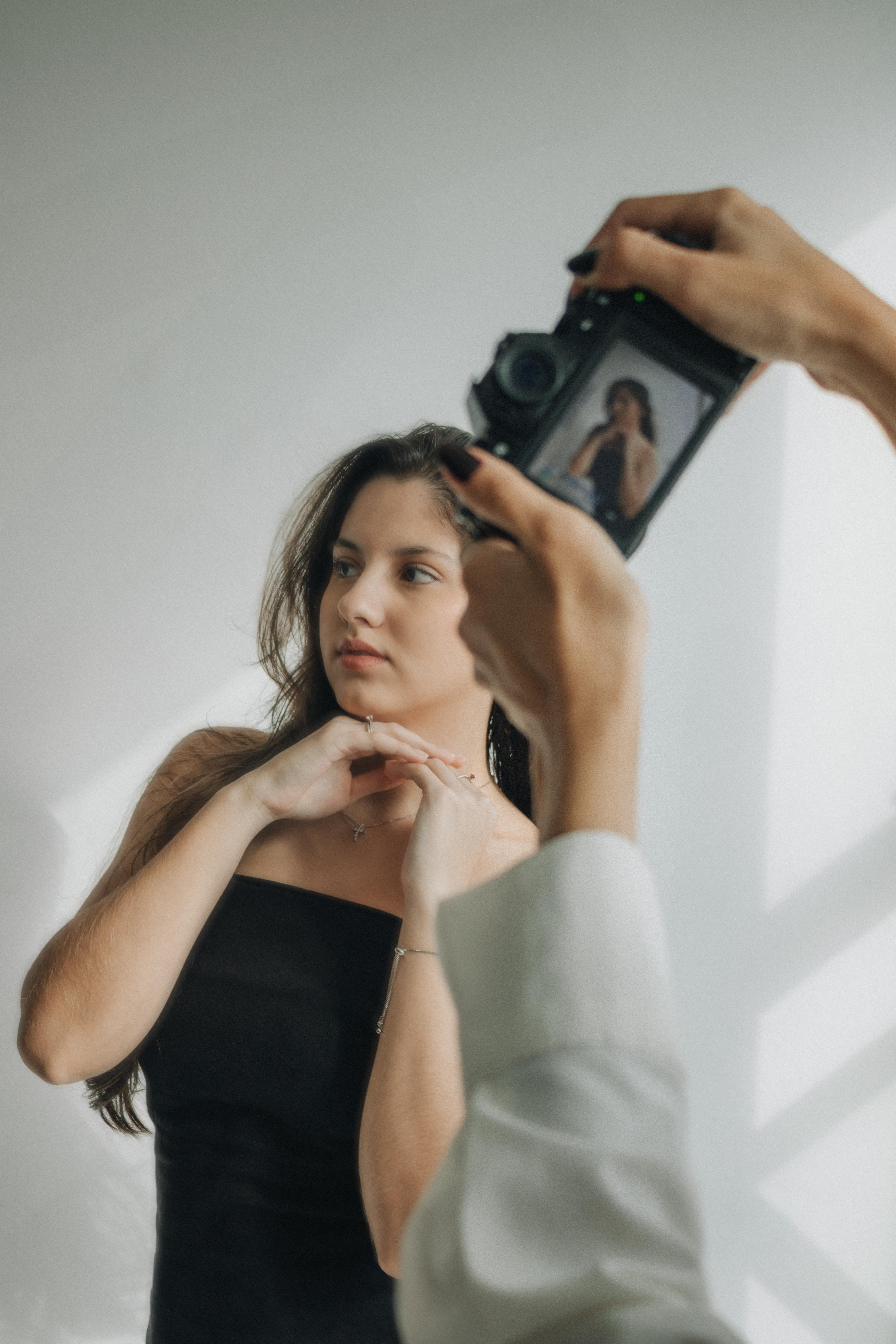 A studio photographer captures a young adult woman posing elegantly against a neutral backdrop.