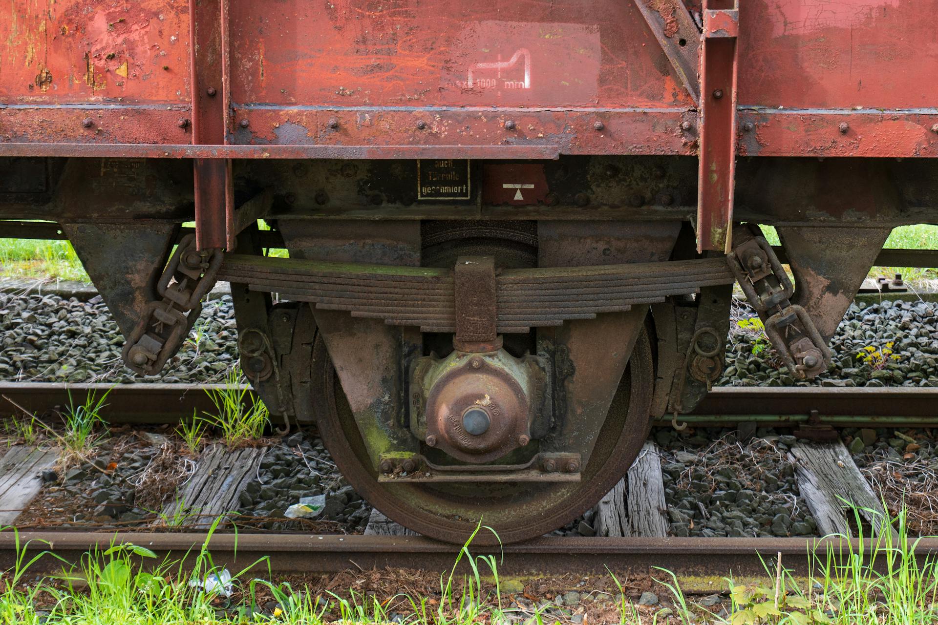 Detailed shot of a rusty train wheel and spring assembly on railway tracks.