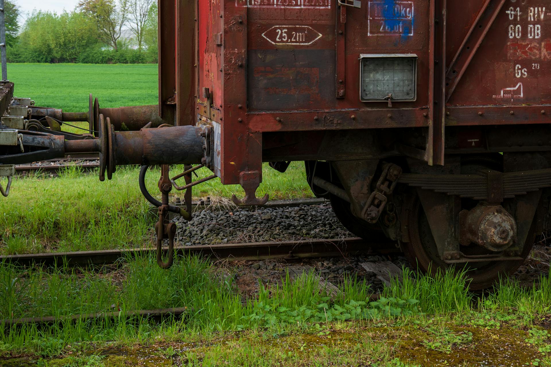 Close-up of a rusty freight train car coupling in a lush green countryside setting.