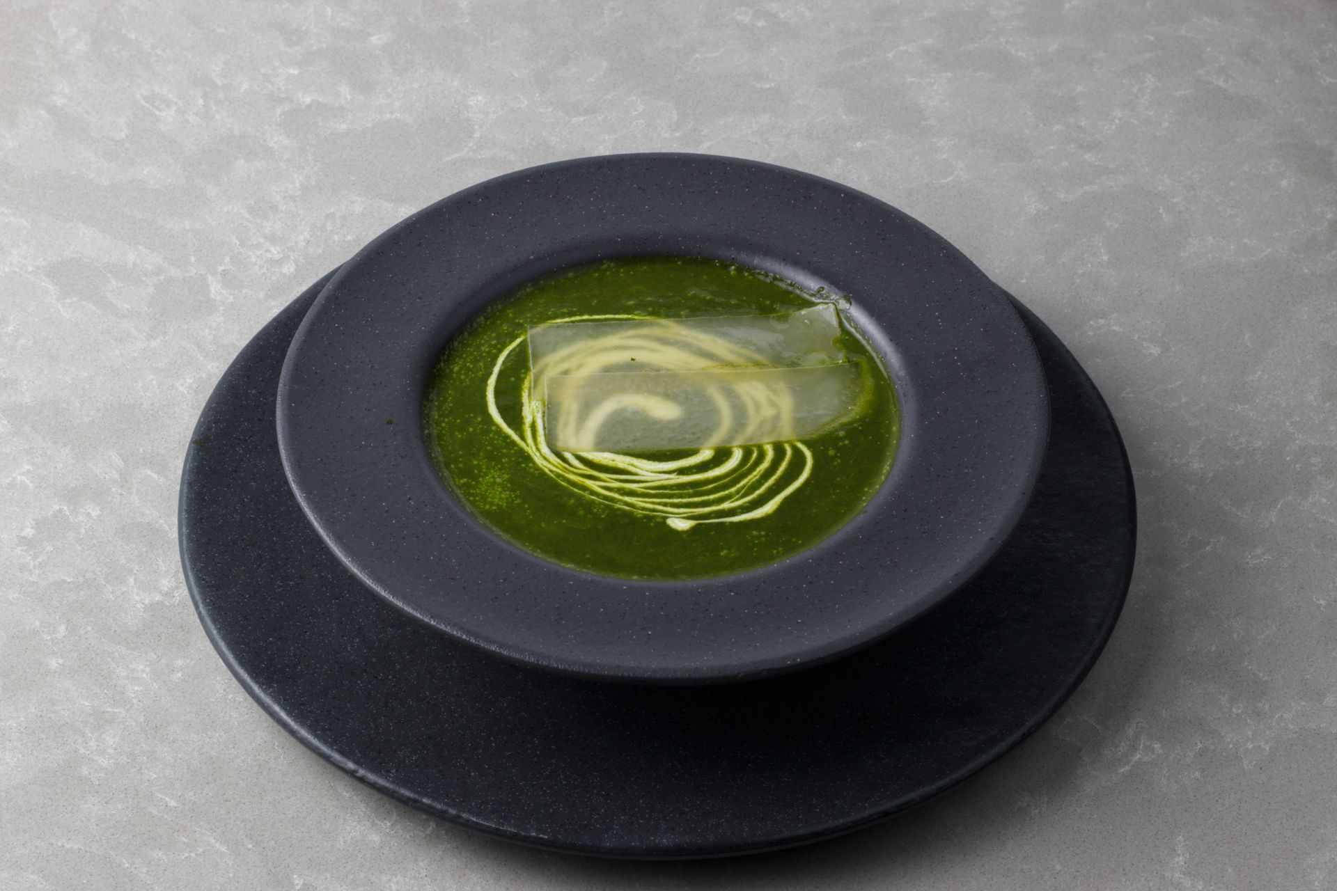 Top-down view of a vibrant green spinach soup with creamy swirl, served in a black bowl on a gray surface.